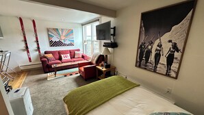Ein modernes Hotelzimmer mit einem großen Bett, einem roten Sofa, einem Fernseher und einem Wandbild mit Ski-Motiv.
