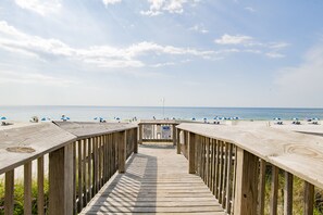 Een houten looppad dat naar een strand leidt, met parasols en ligstoelen.