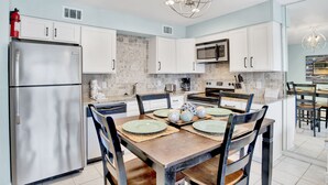 Una cocina moderna con armarios blancos, un refrigerador de acero inoxidable, un microondas y una mesa de comedor lista para cuatro personas.