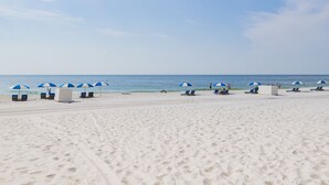 Una playa de arena blanca, sombrillas azules y sillas de descanso.