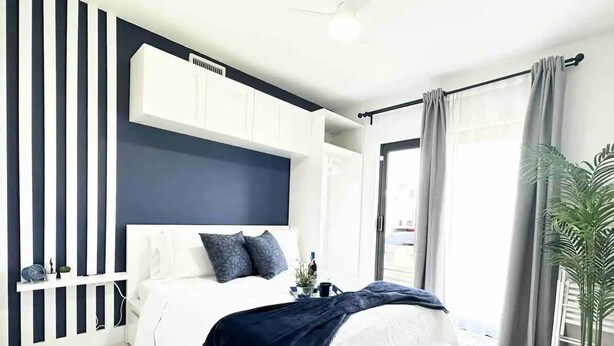A modern bedroom with a large bed, a white wardrobe, a dark headboard, and a potted plant. - Luxurious Blue Studio! The Keys, Everglades, Biscayne N. Park, Redlands & Miami (Florida City)