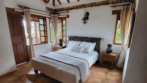 Un dormitorio con una cama grande, vigas de madera en el techo y suelo de baldosas.