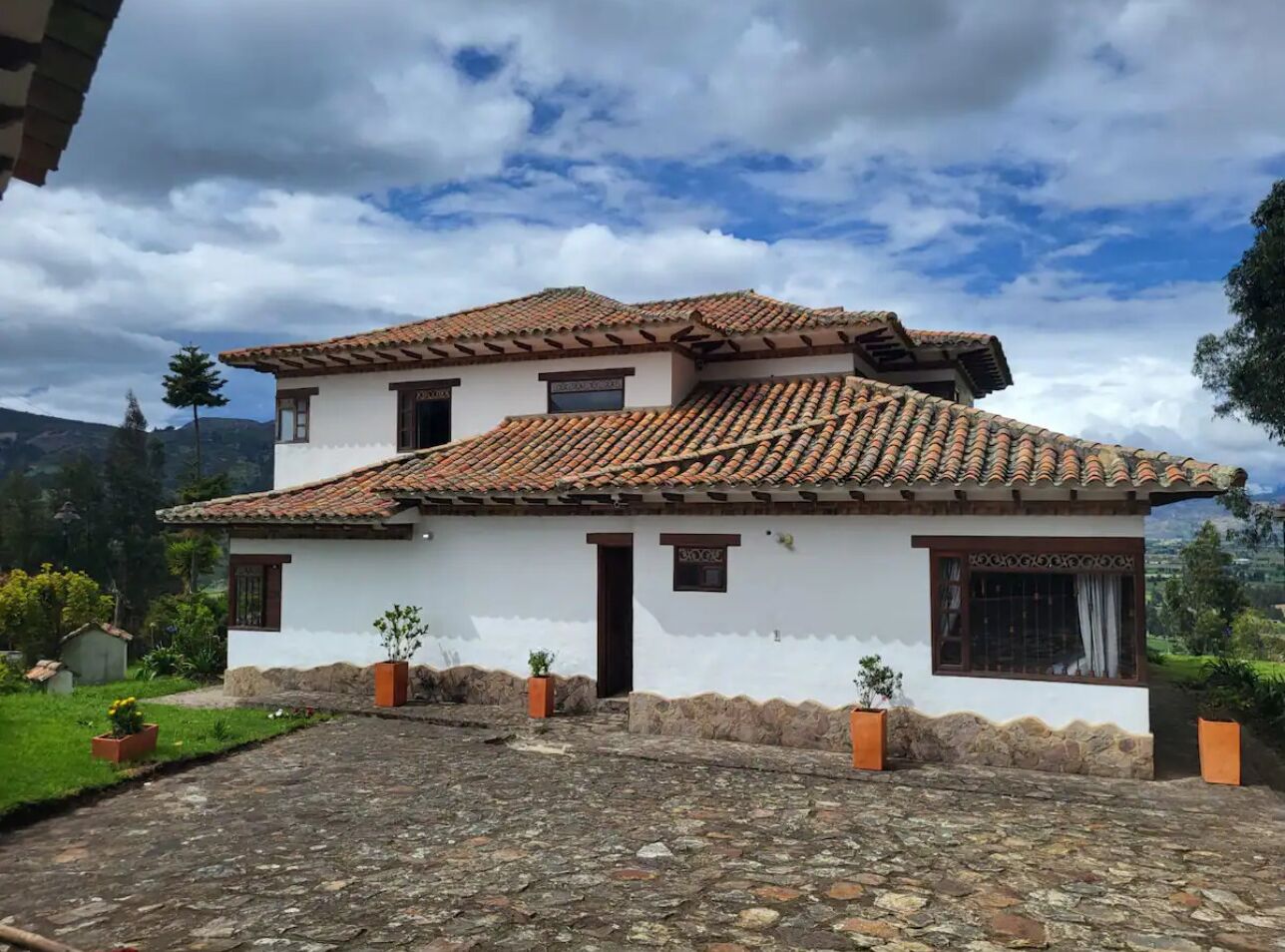 A two-story house with a tiled roof, white walls, and a stone foundation.