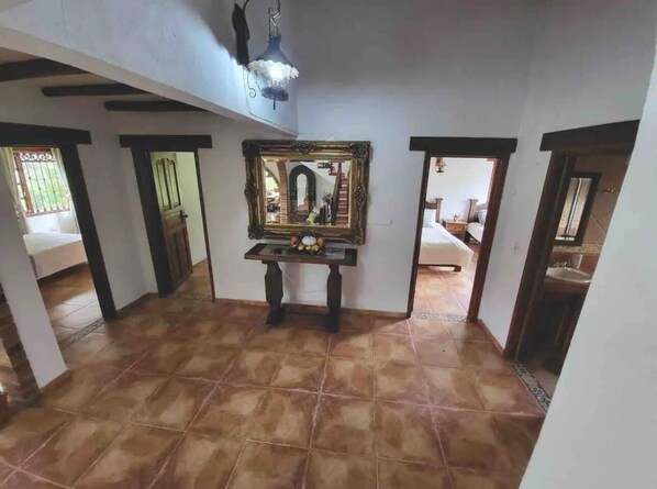 Una habitación amplia con suelo de baldosas, un espejo grande sobre un tocador de madera oscura y una lámpara en el techo.