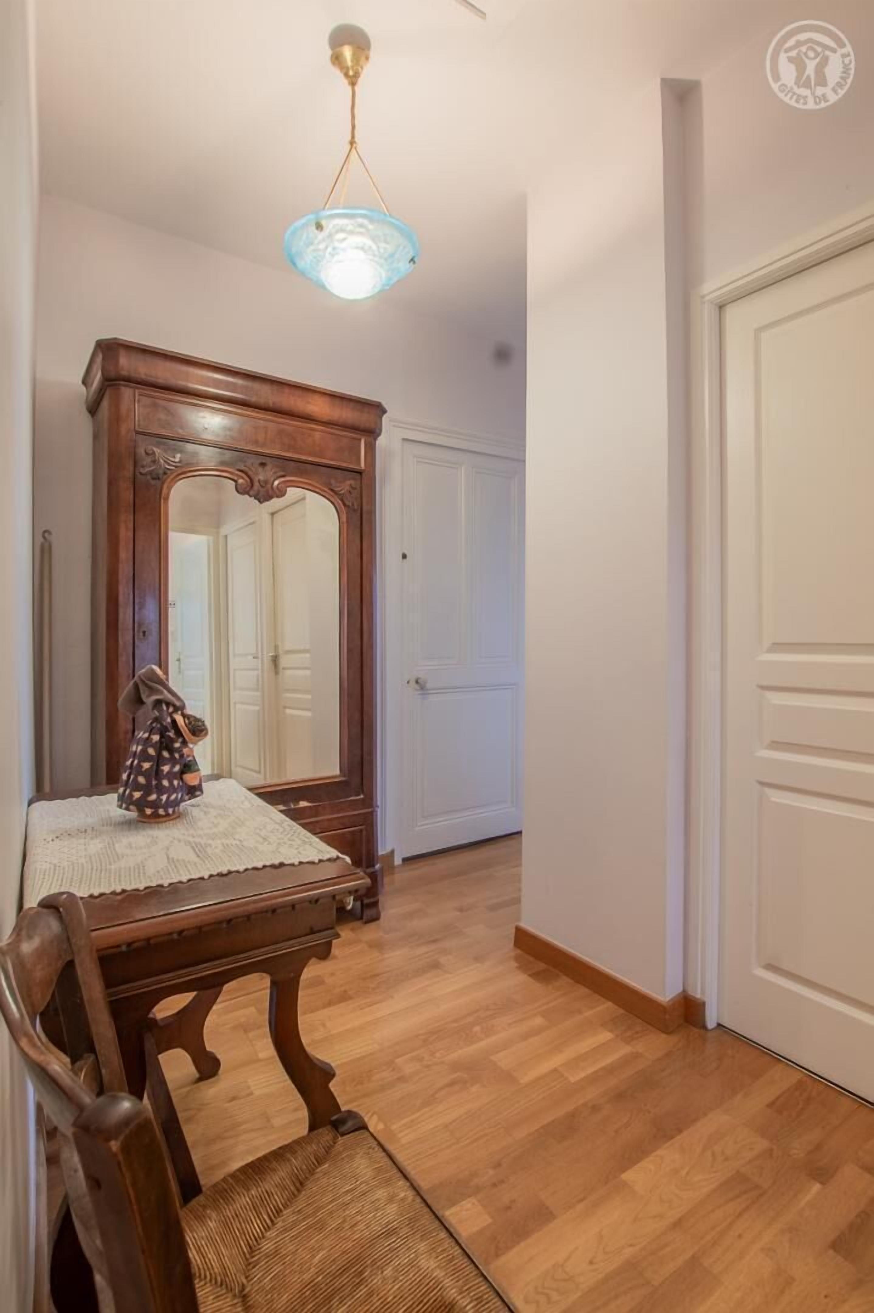 Un couloir avec une table à manger en bois, des chaises, un grand miroir et un luminaire suspendu.