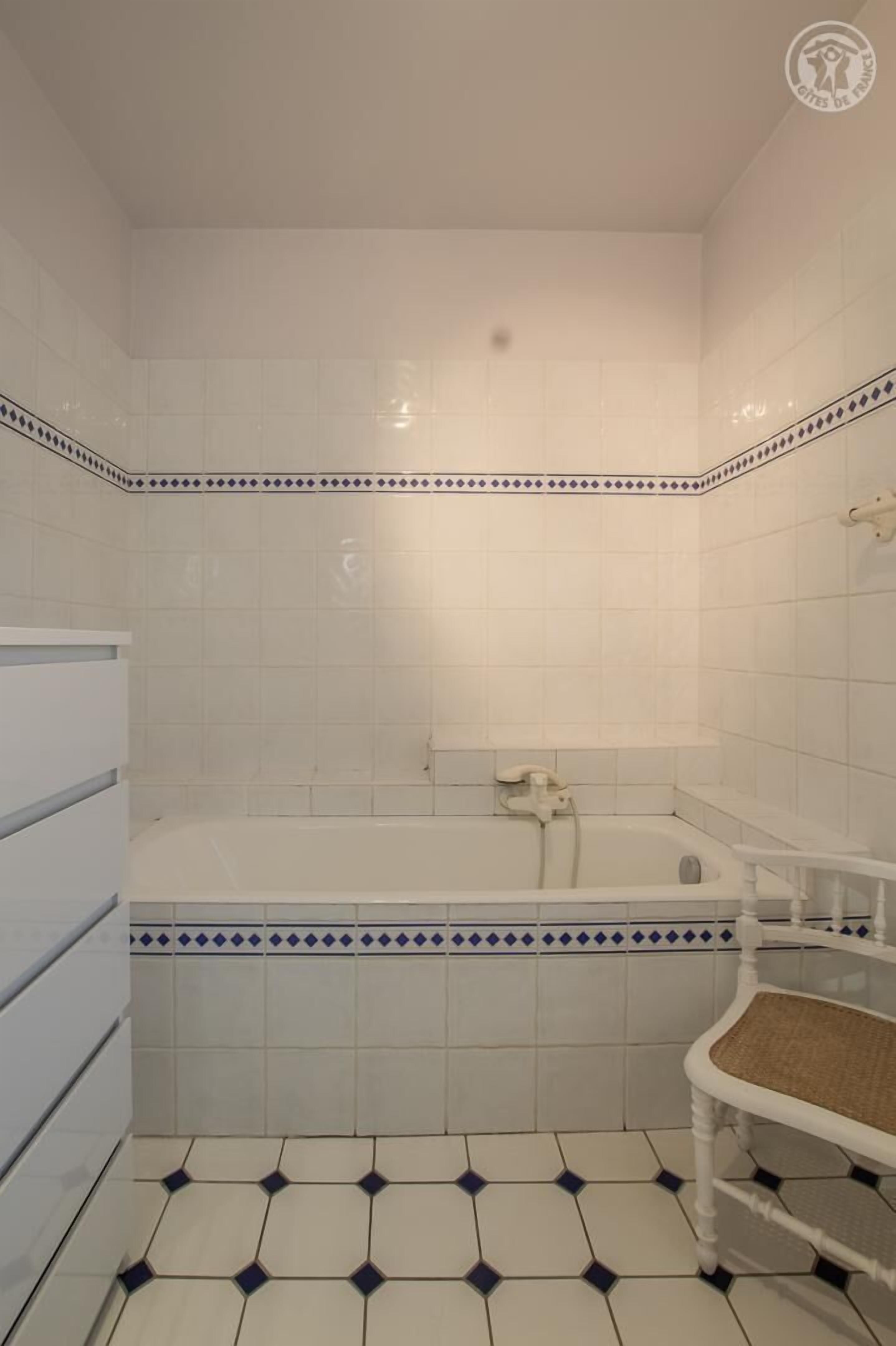 A bathroom with a bathtub, white tiled walls, and a patterned floor.