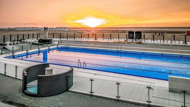Una piscina en la azotea con vistas al atardecer, sillas de descanso y una pequeña piscina circular.