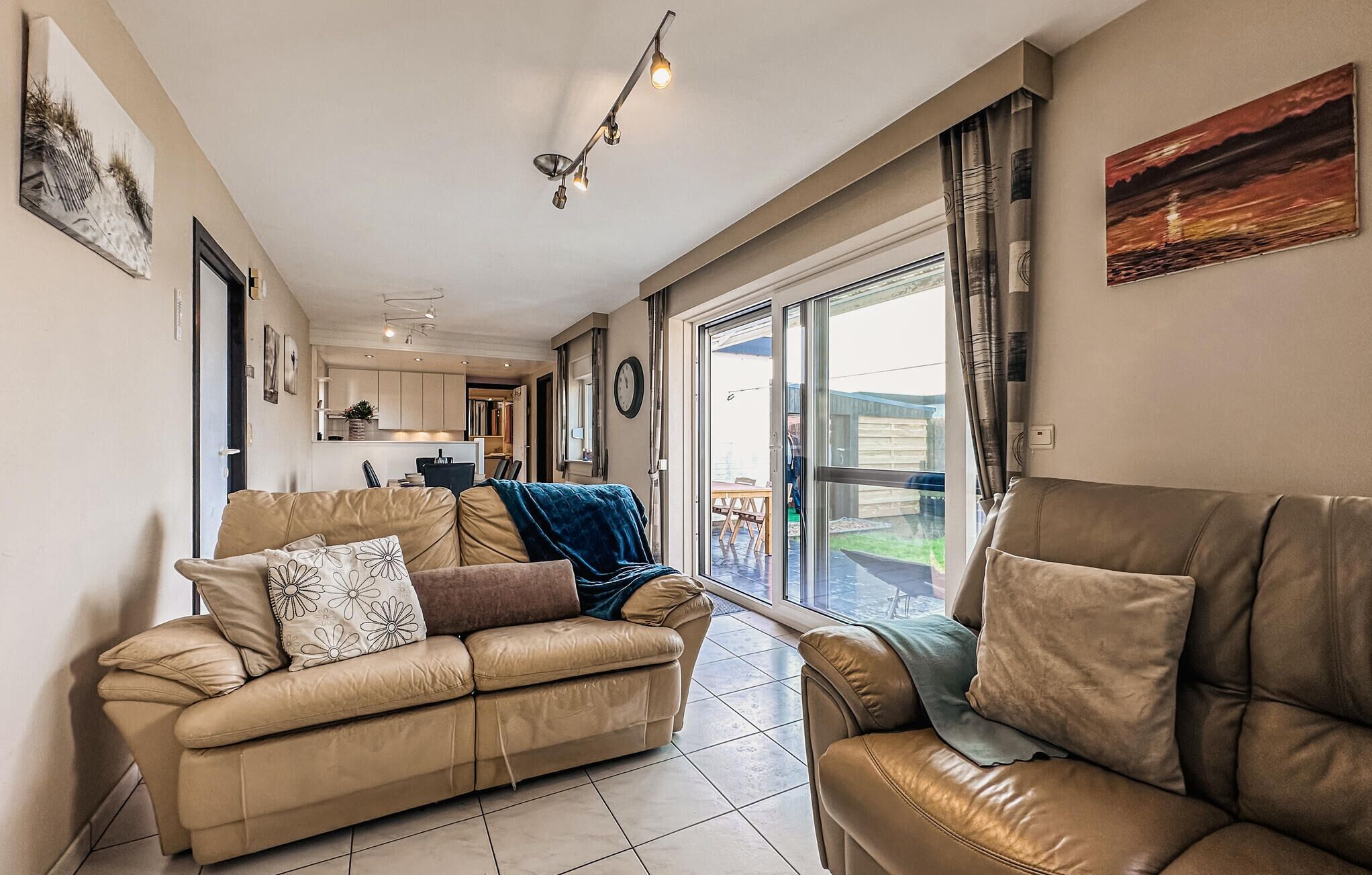 A spacious living room with a beige leather sofa, a dining area with a table and chairs, and a large sliding glass door leading to a patio.