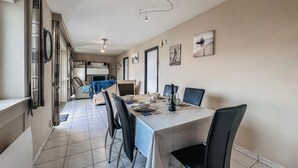 Un comedor con una mesa dispuesta para cuatro personas, sillas, un sofá y un televisor al fondo.