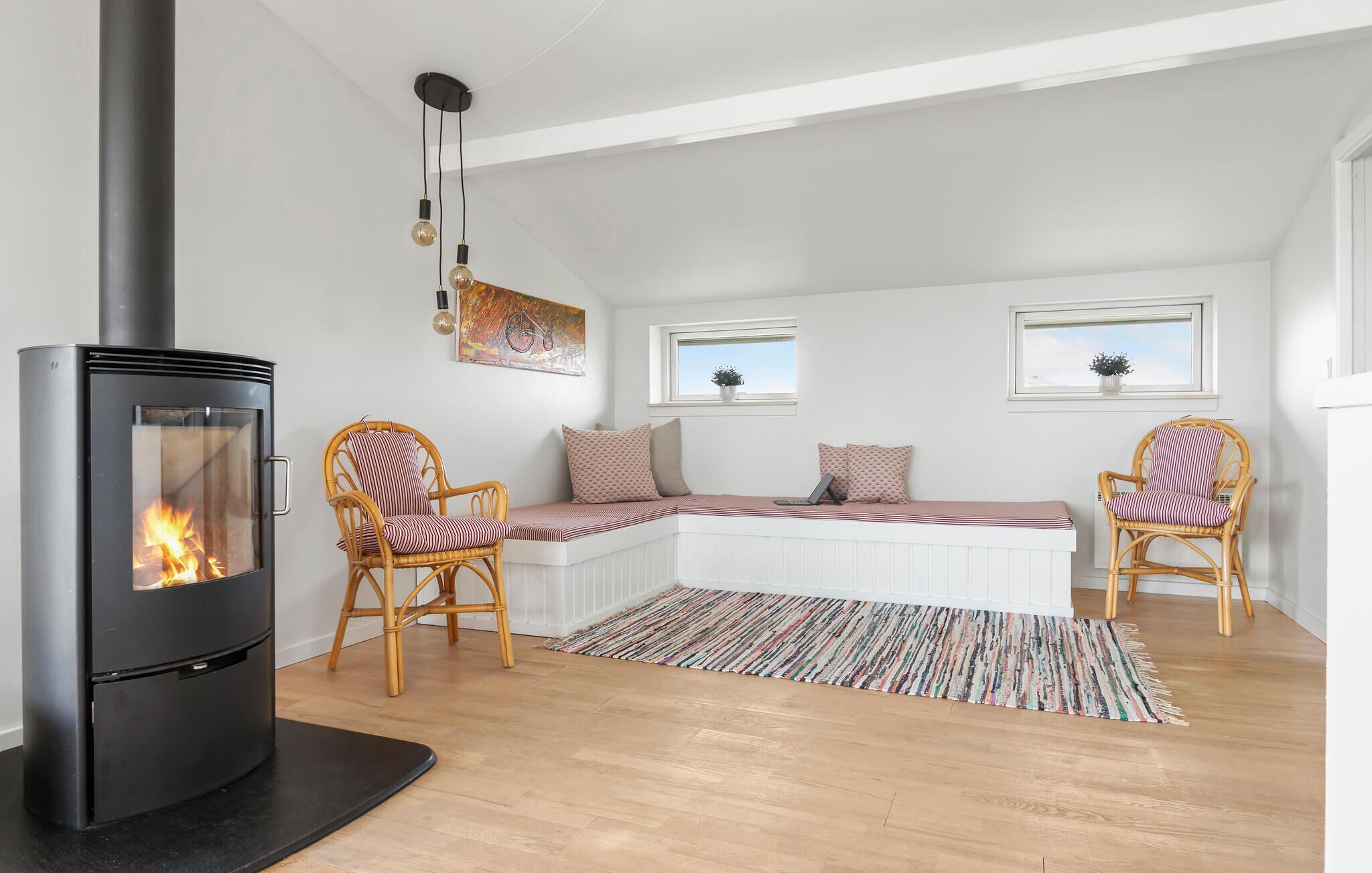 A cozy room with a black wood-burning stove, two wicker chairs, a bench with cushions, and a colorful rug.