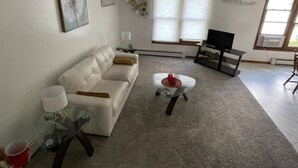 A living room with a white sofa, a glass coffee table, a TV on a stand, and a wall with a 'Family Forever' sign. - Private Lake House on Pokegama in northern MN. For any occasion all year round. (Grand Rapids)