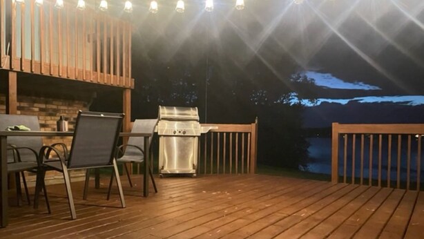 A wooden deck with a grill and chairs, a table, and a railing. - Private Lake House on Pokegama in northern MN. For any occasion all year round. (Grand Rapids)
