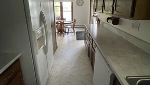 A narrow kitchen with a refrigerator, cabinets, and a dining area with chairs and a table. - Private Lake House on Pokegama in northern MN. For any occasion all year round. (Grand Rapids)