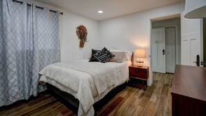 Ein Schlafzimmer mit Bett, Nachttisch, Lampe und einer Tür zu einem anderen Raum.