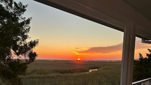 A wooden deck with a railing overlooking a natural landscape during sunset.