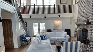 A spacious living room with a white sectional sofa, a striped armchair, and a fireplace.