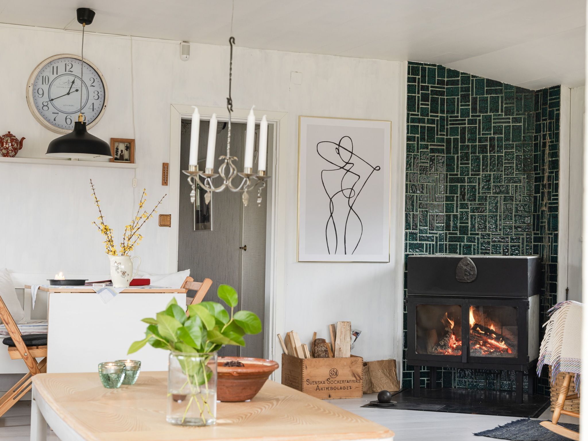 Ein Wohnzimmer mit Kamin, einer Essecke mit Tisch und Stühlen, einer Wanduhr und einer grünen Fliesenwand.