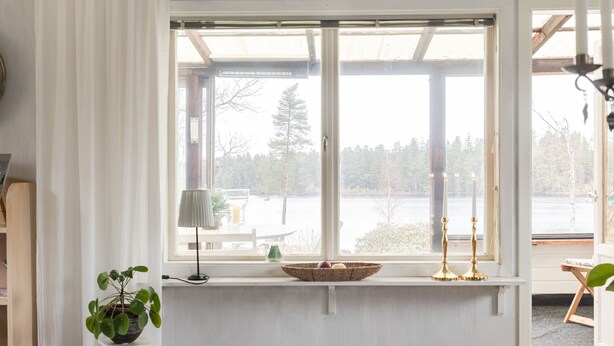 Ein Zimmer mit großem Fenster mit Blick auf einen See, einem kleinen Tisch mit Lampe und einem Regal mit Dekorationen.