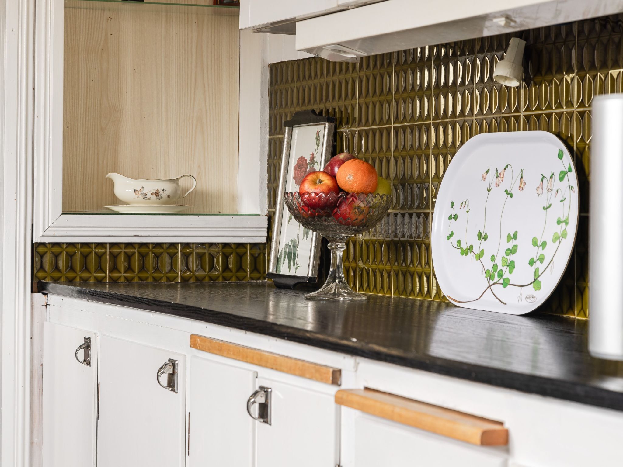 Un comptoir de cuisine avec un panier de fruits, une assiette décorative et un meuble avec une poignée.