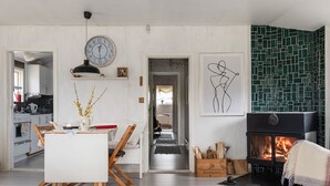 Ein modernes Wohnzimmer mit Kamin, einer Essecke mit weißem Tisch und Stühlen, einer durchgehenden Tür erkennbaren Küche und einer Wand mit grünem Muster.