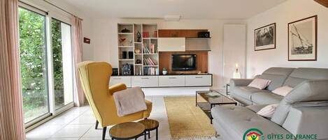 Een moderne woonkamer met een bank, fauteuil, televisie en boekenkast.