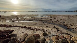 Une plage avec un rivage rocheux au premier plan et une eau calme à l’arrière-plan.