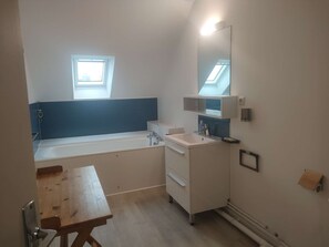A modern bathroom with a bathtub, a sink, and a mirror. There is a skylight above the bathtub and a small window.
