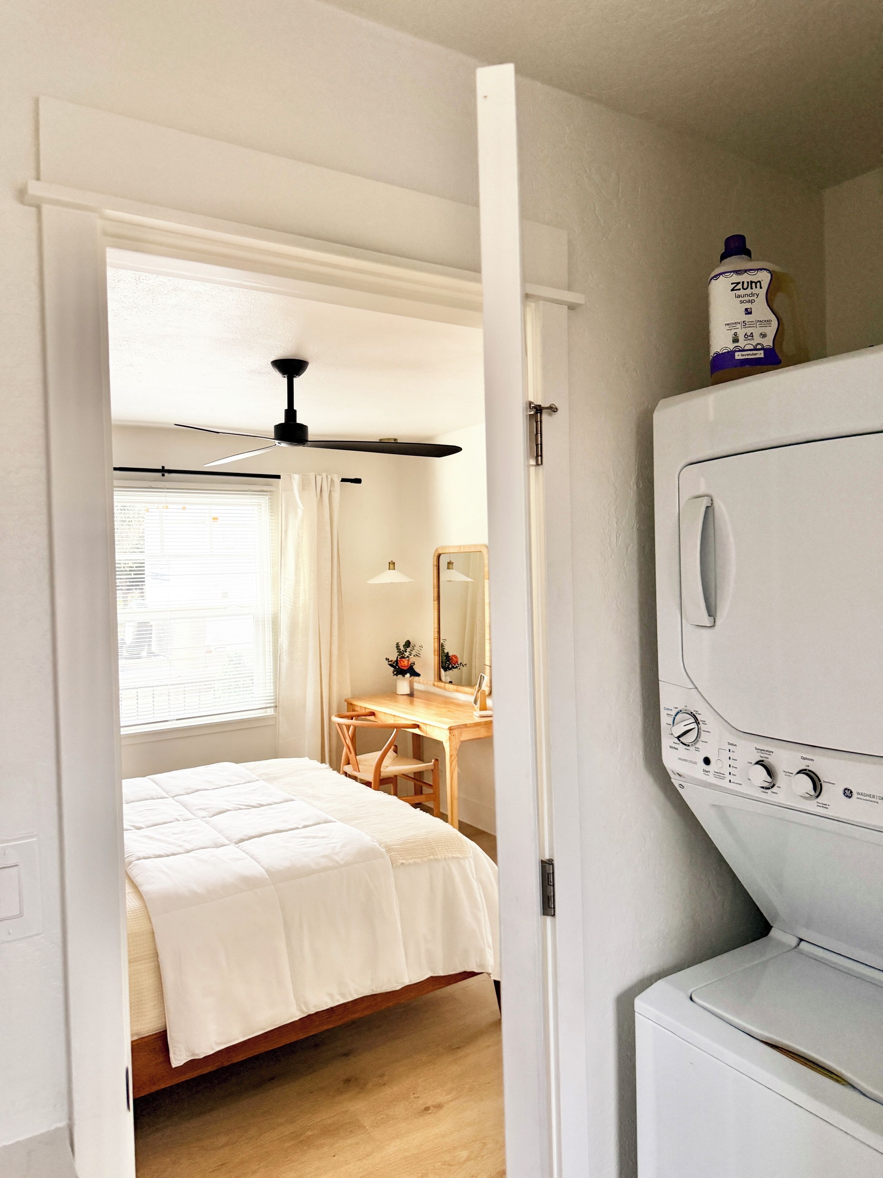 A bedroom with a bed, a desk, a mirror, and a washing machine.