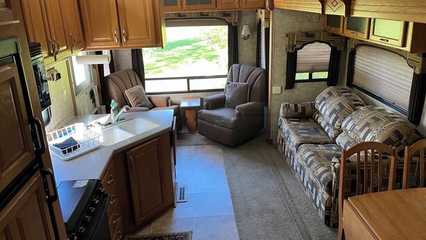 A compact RV interior with a kitchenette, a dining area, and a seating area with a sofa and chairs.