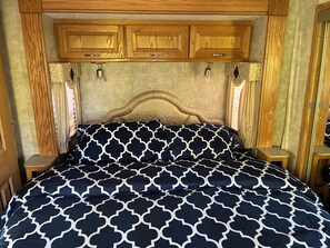 A bedroom with a wooden headboard, a patterned bedspread, and two bedside lamps. - Hummingbird - Camper at Sunset Bay  (Onanole)
