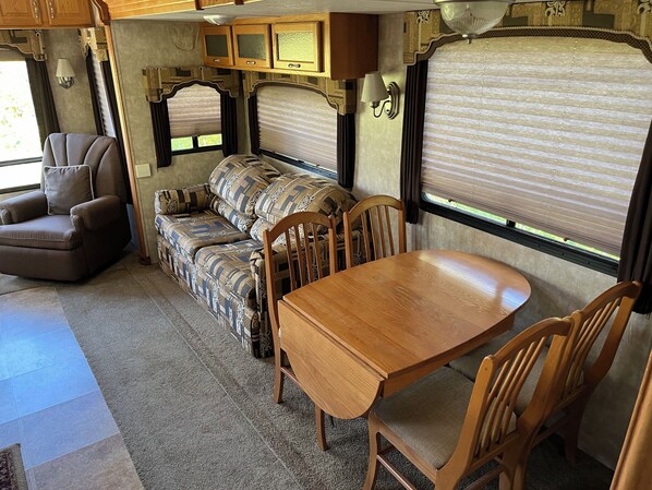 A cozy RV interior with a sofa, chair, dining table, and built-in cabinets. - Hummingbird - Camper at Sunset Bay (Onanole)