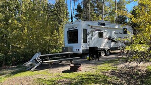 A recreational vehicle (RV) parked in a wooded area with a picnic table and a grill.