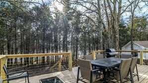 A wooden deck with a table and chairs, surrounded by trees. - LAKEFRONT Bliss FLAT to water: Spacious home with Game Room, Sleeps 15 Guests!  (Garfield)