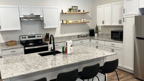 A modern kitchen with white cabinets, a granite countertop, a stainless steel refrigerator, and a bar sign above a shelf. - LAKEFRONT Bliss FLAT to water: Spacious home with Game Room, Sleeps 15 Guests!  (Garfield)