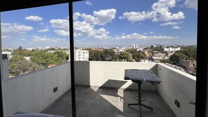 A balcony with a view of a cityscape, a table with a black cover, and a chair. - Excelente Alojamiento en la Cdmx (Ciudad de México)