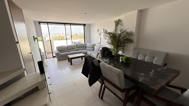 A modern living room with a large sectional sofa, a dining table, and a staircase leading to an upper floor. - Excelente Alojamiento en la Cdmx (Ciudad de México)
