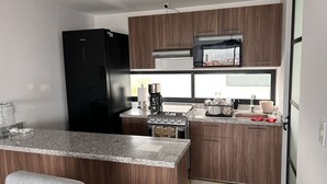 A modern kitchen with a black refrigerator, a stove, and a coffee maker. There is a window above the sink and a countertop with a basket of dishes. - Excelente Alojamiento en la Cdmx (Ciudad de México)
