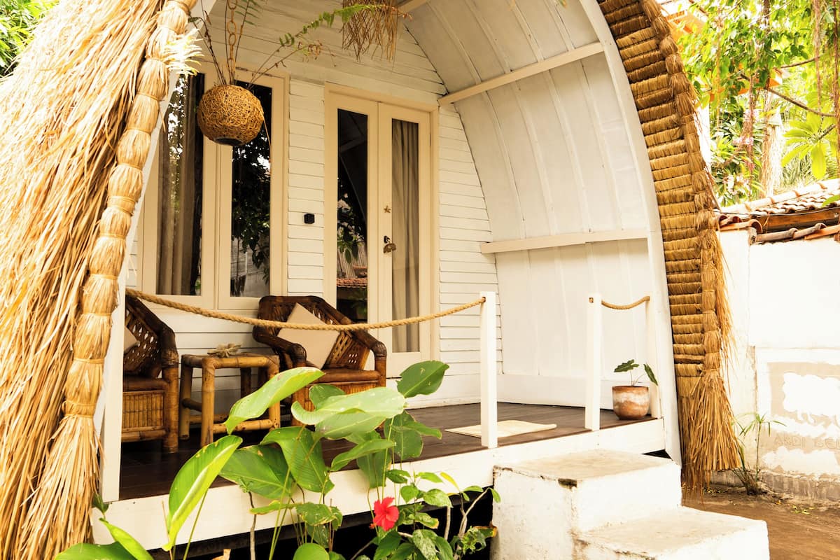 A white house with a thatched roof, a porch with chairs, and a hanging basket.