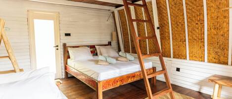 A loft-style bedroom with a wooden ladder, a bed with white linens, and a woven wall panel.