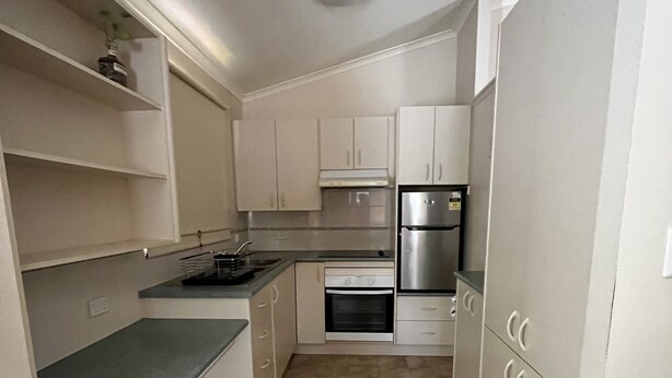 A compact kitchen with white cabinets, a stainless steel refrigerator, and a built-in oven. - Beachmere Dude Ranch (Beachmere)