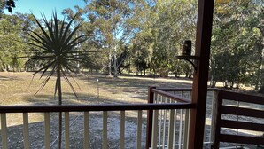 A wooden deck with a railing, overlooking a park with trees and a large, star-shaped sculpture. - Beachmere Dude Ranch (Beachmere)