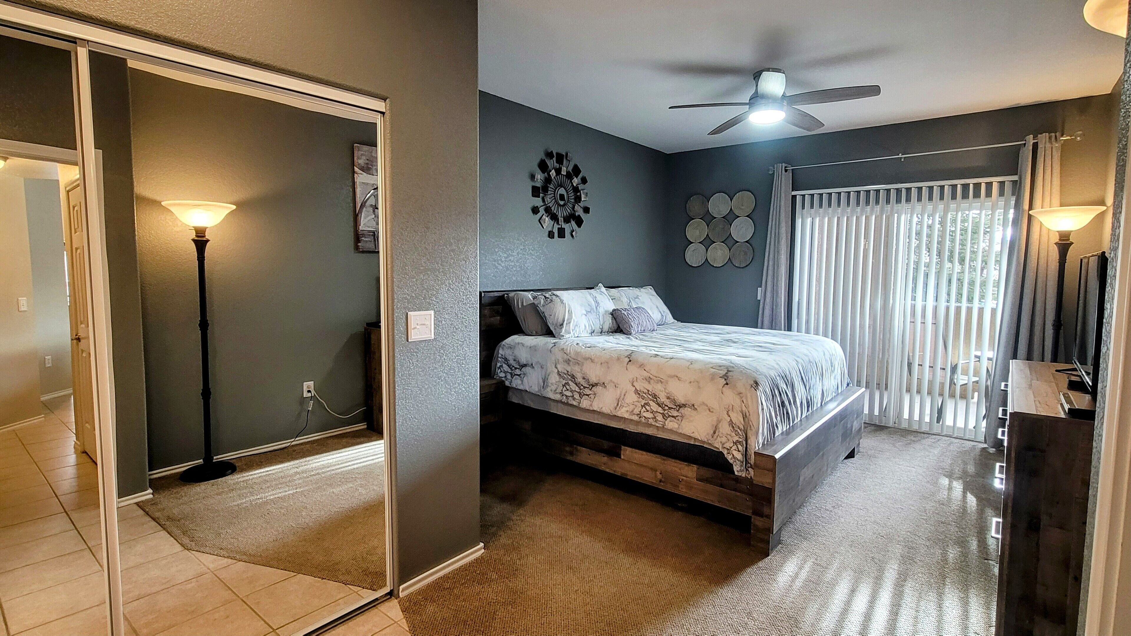 A bedroom with a bed, a ceiling fan, a window with curtains, and a wall clock.
