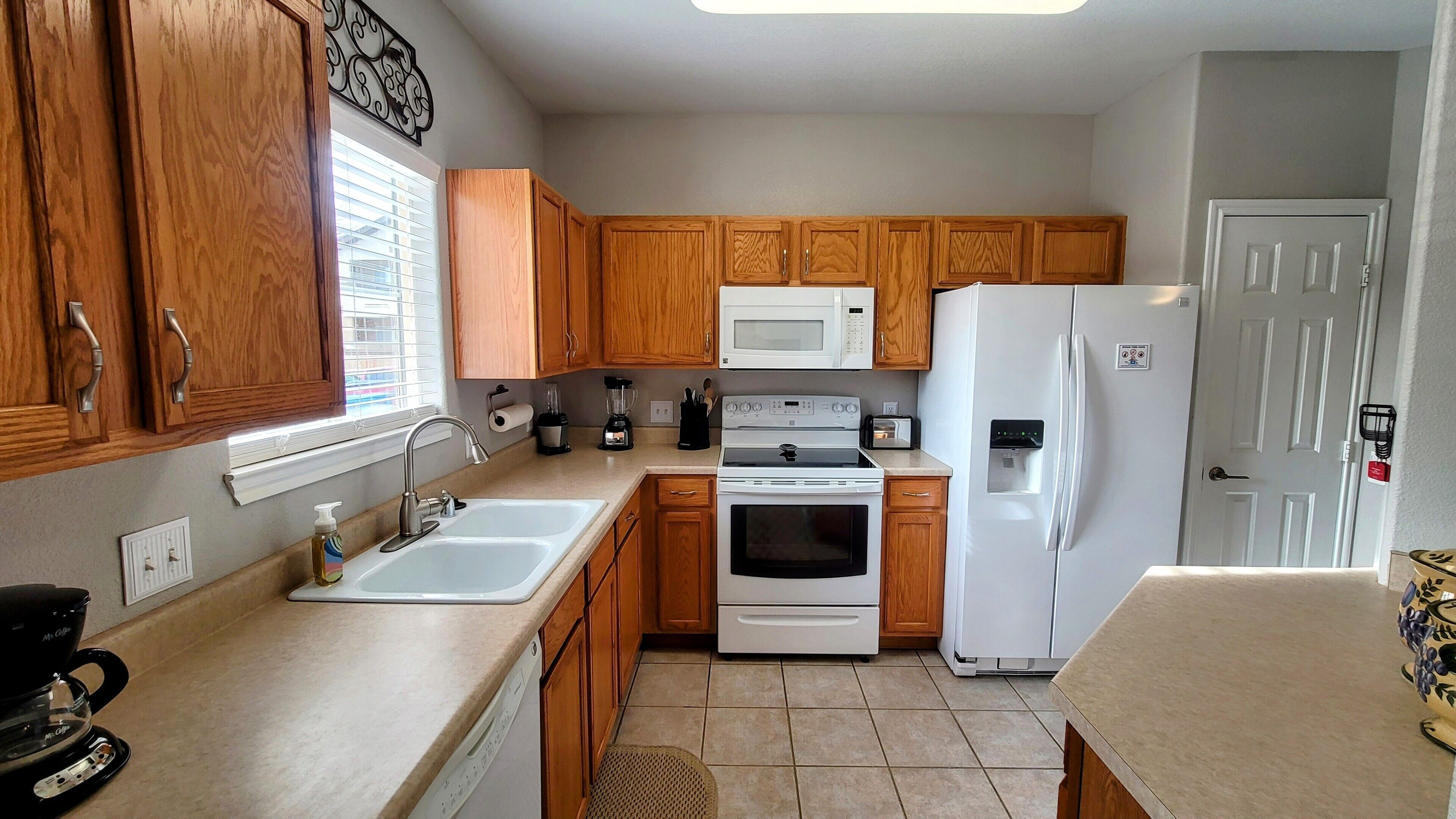 A compact kitchen with wooden cabinets, a white refrigerator, a microwave, an oven, and a coffee maker.