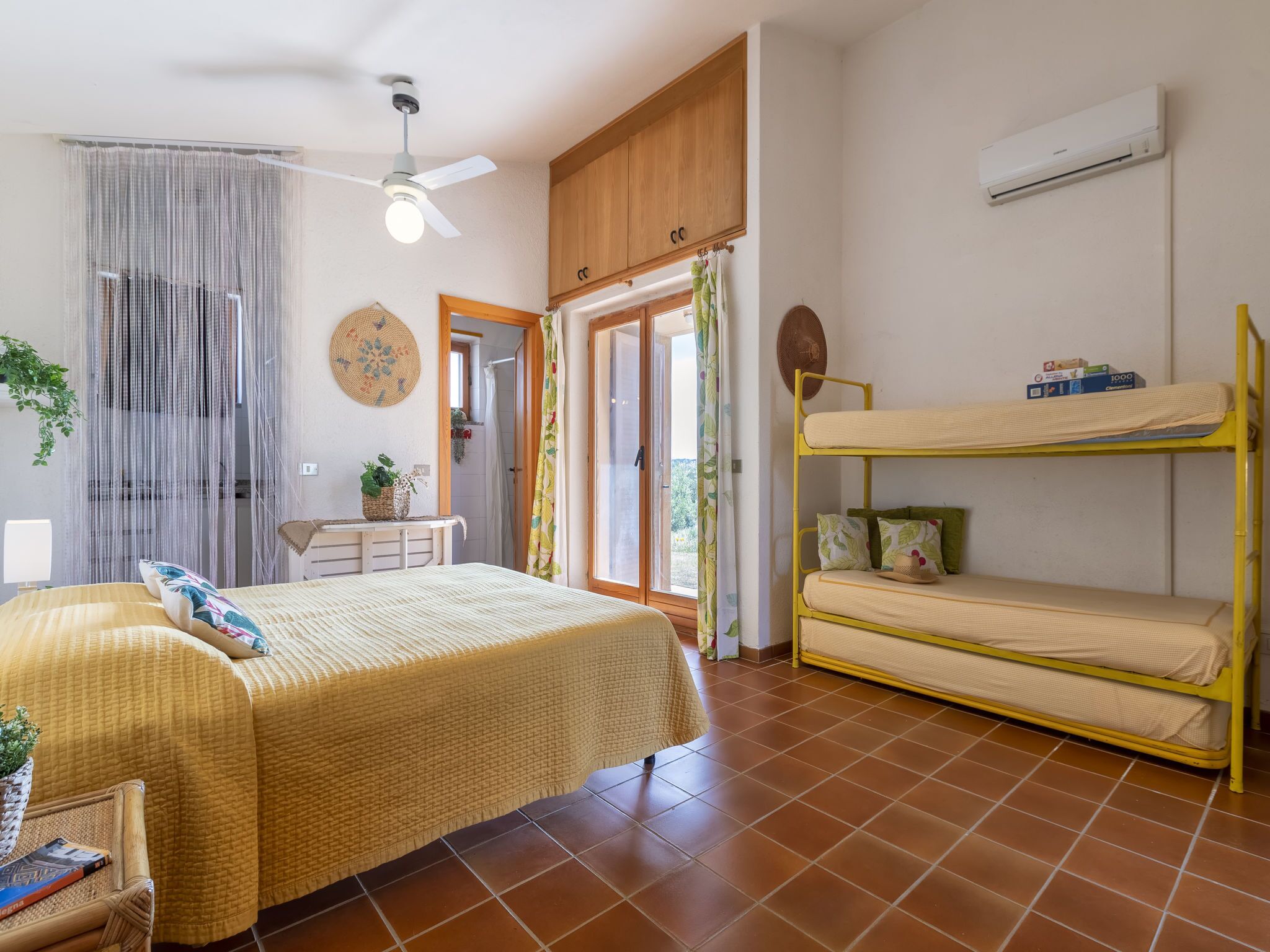 A bedroom with a bed, a bunk bed, a ceiling fan, an air conditioner, and a view of the outdoors.