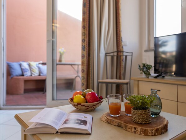 A room with a table set for breakfast, including a bowl of fruit, two glasses of orange juice, and a book.