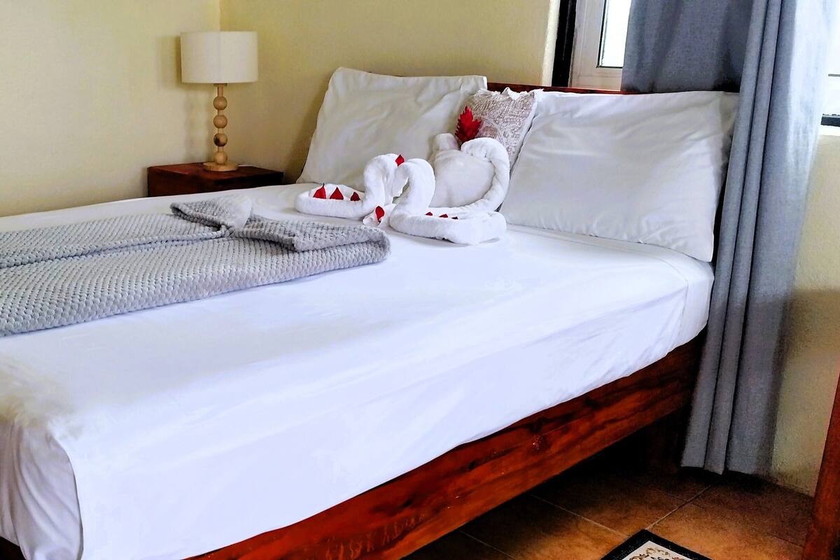 A neatly made bed with a folded blanket, a decorative swan pillow, and a lamp on a bedside table.