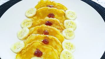 Uma pilha de panquecas com fatias de banana e frutas vermelhas numa travessa branca, colocada sobre uma mesa com borda preta.