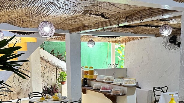 A dining area with a thatched ceiling, black chairs, a wooden counter, and a green wall in the background. - Carpe Diem (Cairu)