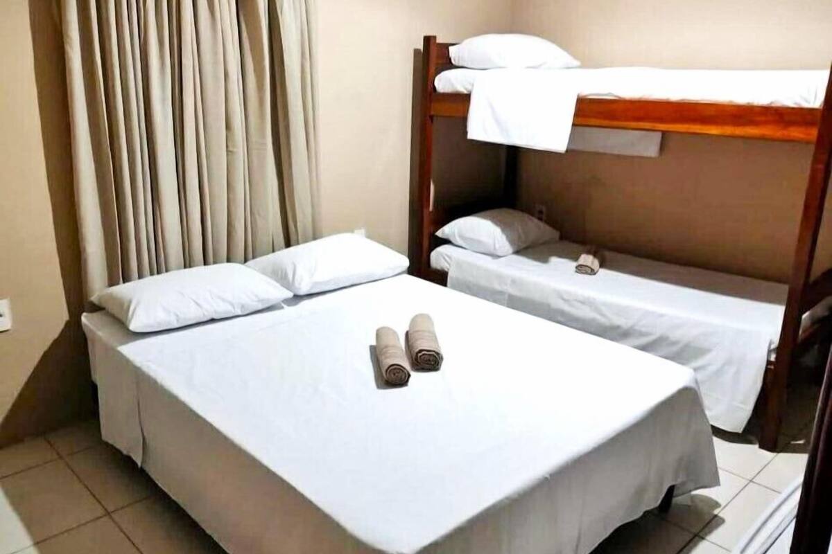 A room with two beds, one with a wooden headboard and the other with a plain headboard. There are two rolled towels on the bed with the wooden headboard.