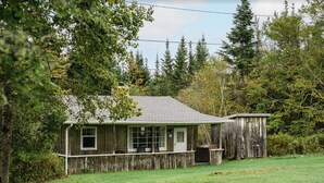 A rustic wooden house with a porch, surrounded by trees and a grassy yard. - Log Cabin #1 - Hubbards Beach (Hubbards)